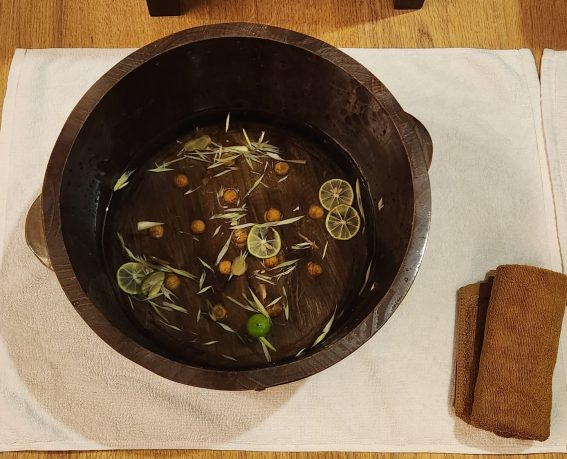 A sink made from wood with warm water and sliced lemongrass, lemon and ginger inside for foot bath.