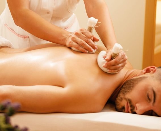 Female therapist using herbal balls while massaging man's back at the spa.