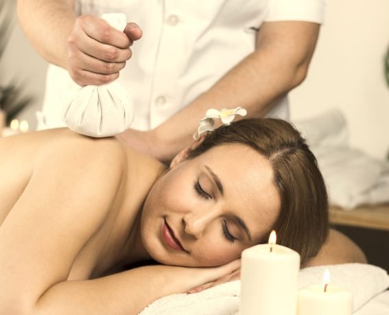 A woman is enjoying an herbal massage in a cozy spa room with multiple burning scented candles.